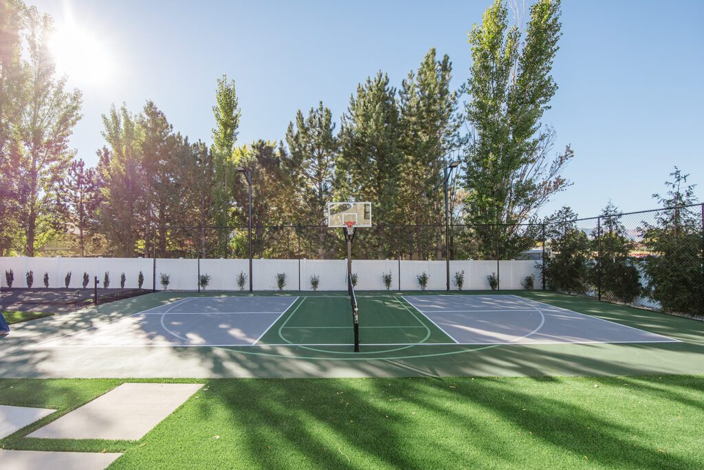 Back exterior of a Utah custom home with sport court, patio space, and beautiful yard design