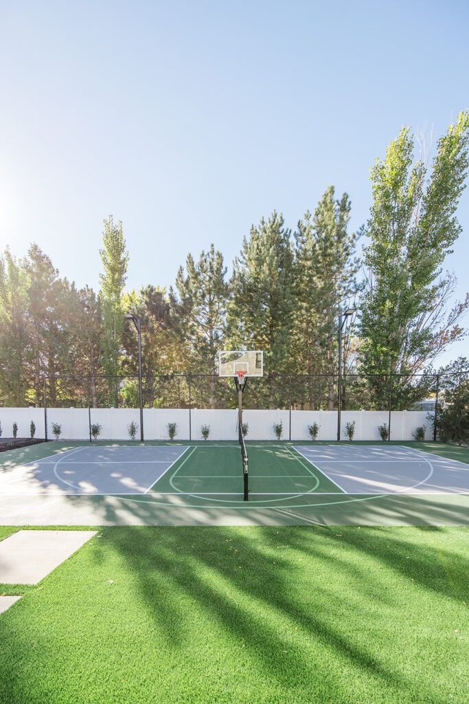 Back exterior of a Utah custom home with sport court, patio space, and beautiful yard design