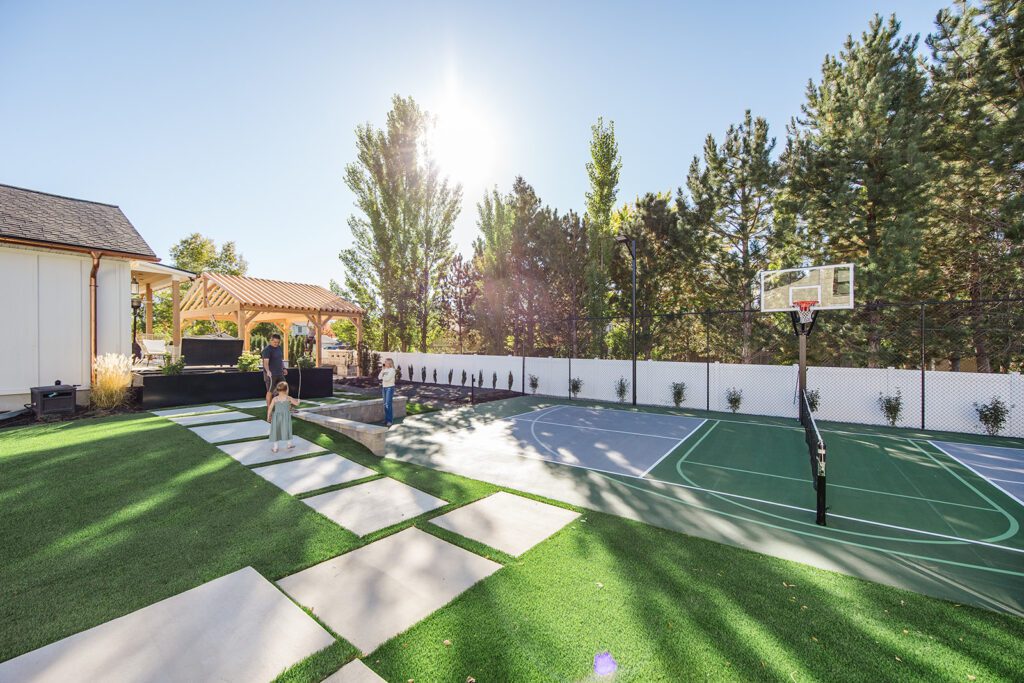 Back exterior of a Utah custom home with sport court, patio space, and beautiful yard design