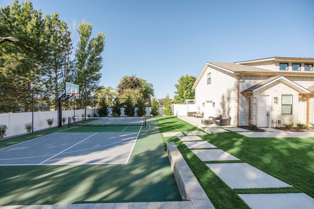 Back exterior of a Utah custom home with sport court, patio space, and beautiful yard design