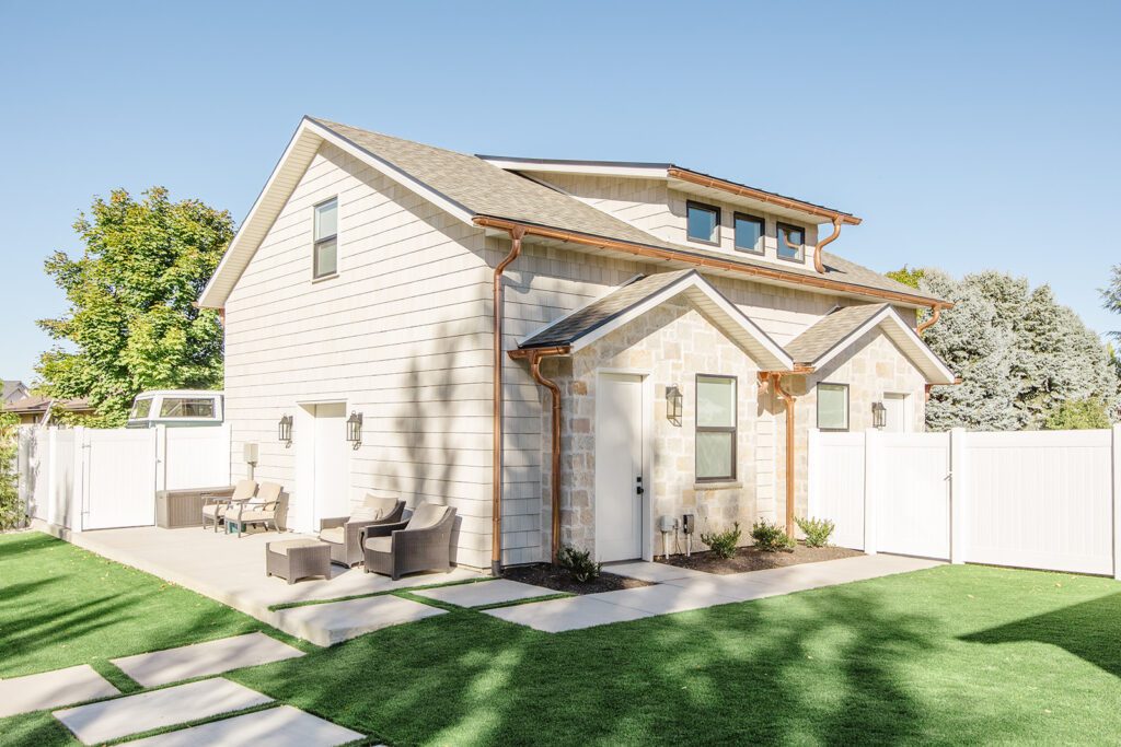 Back exterior of a Utah custom home with sport court, patio space, and beautiful yard design