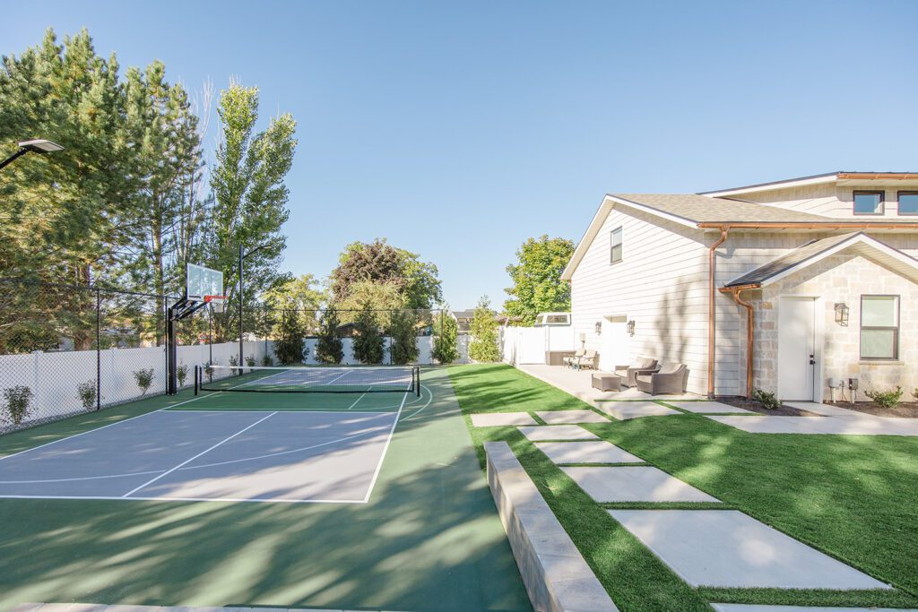Back exterior of a Utah custom home with sport court, patio space, and beautiful yard design