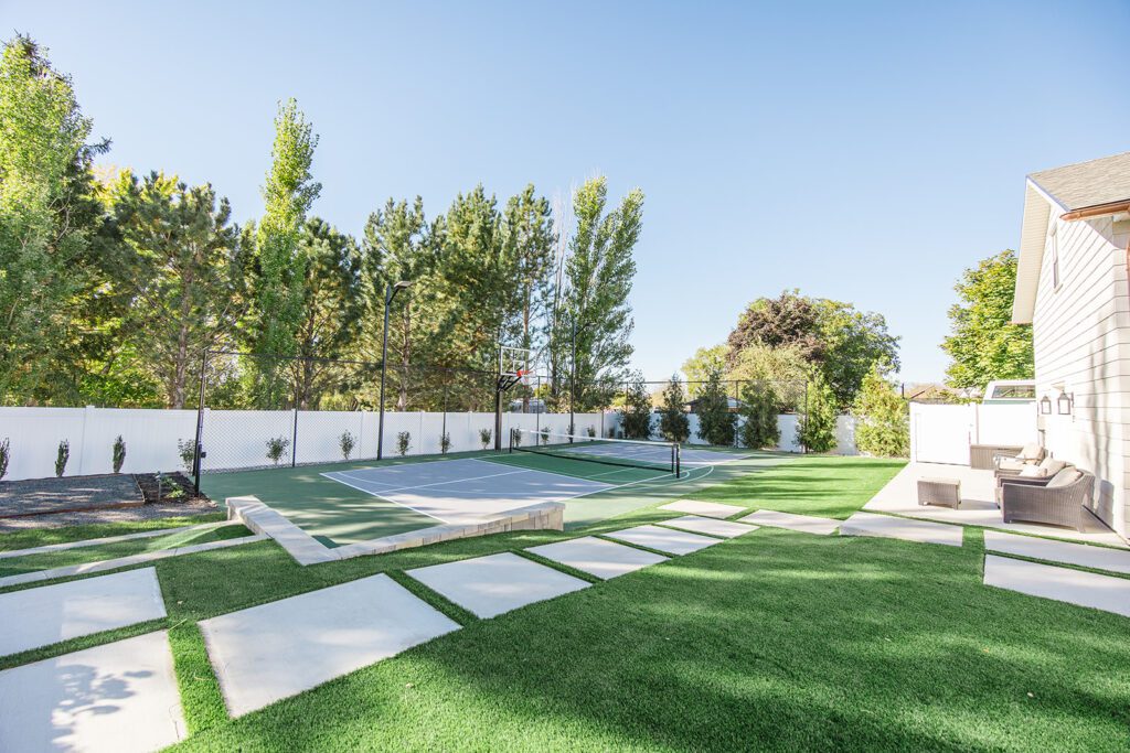 Back exterior of a Utah custom home with sport court, patio space, and beautiful yard design