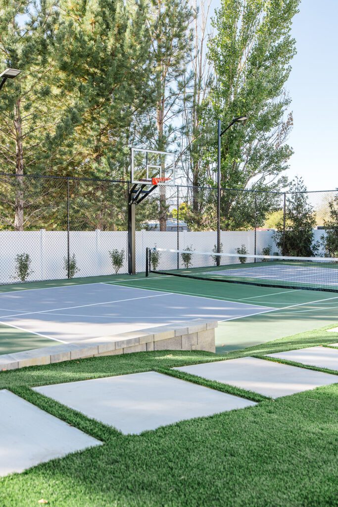 Back exterior of a Utah custom home with sport court, patio space, and beautiful yard design