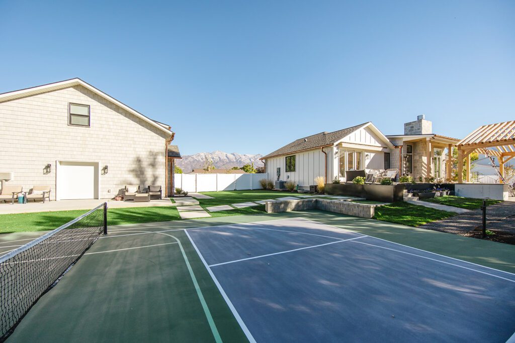 Back exterior of a Utah custom home with sport court, patio space, and beautiful yard design