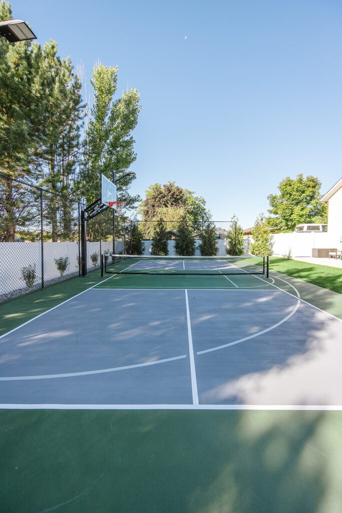 Back exterior of a Utah custom home with sport court, patio space, and beautiful yard design